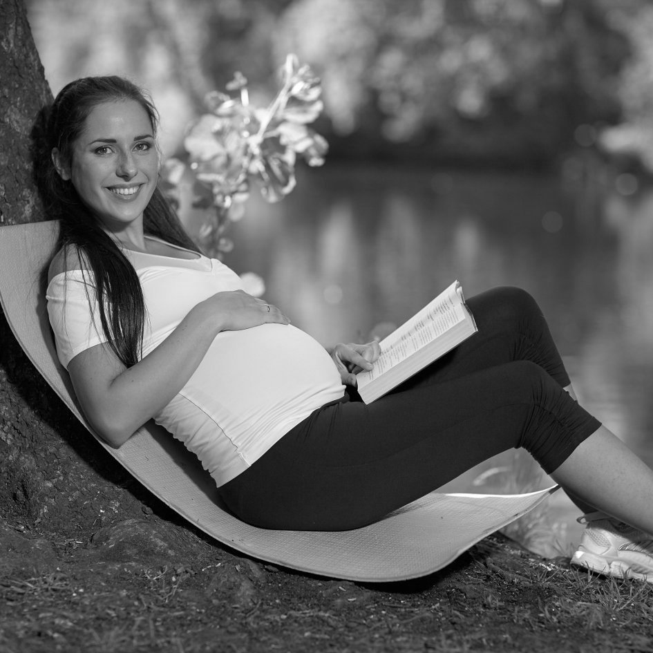 Young beautiful  pregnant  woman with book sits in the park.